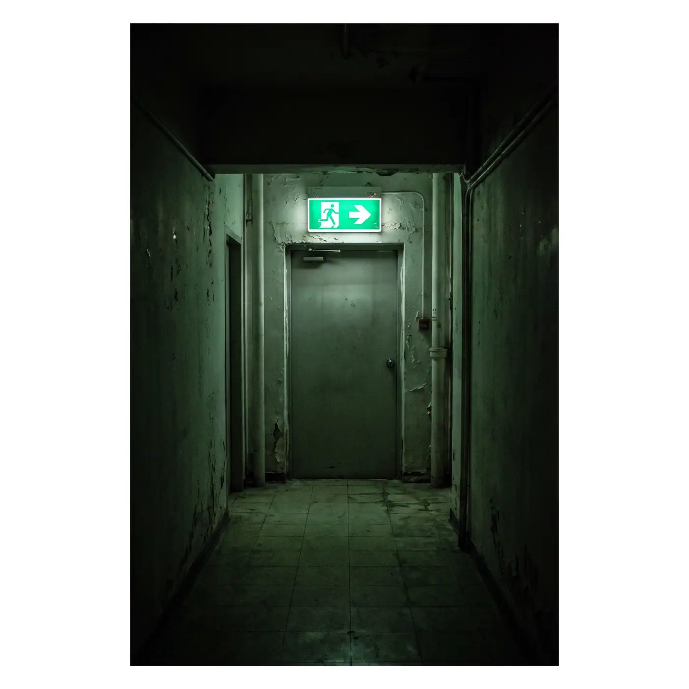 Green illuminated emergency exit sign dark corridor door
