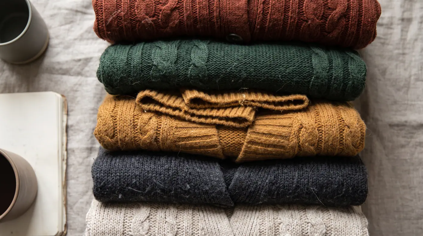 Folded knitwear stack, ribbed cable textures, muted autumn palette
