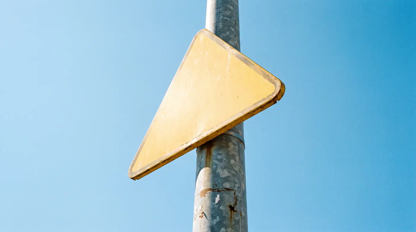 Blank yellow triangular warning sign pole clear blue sky