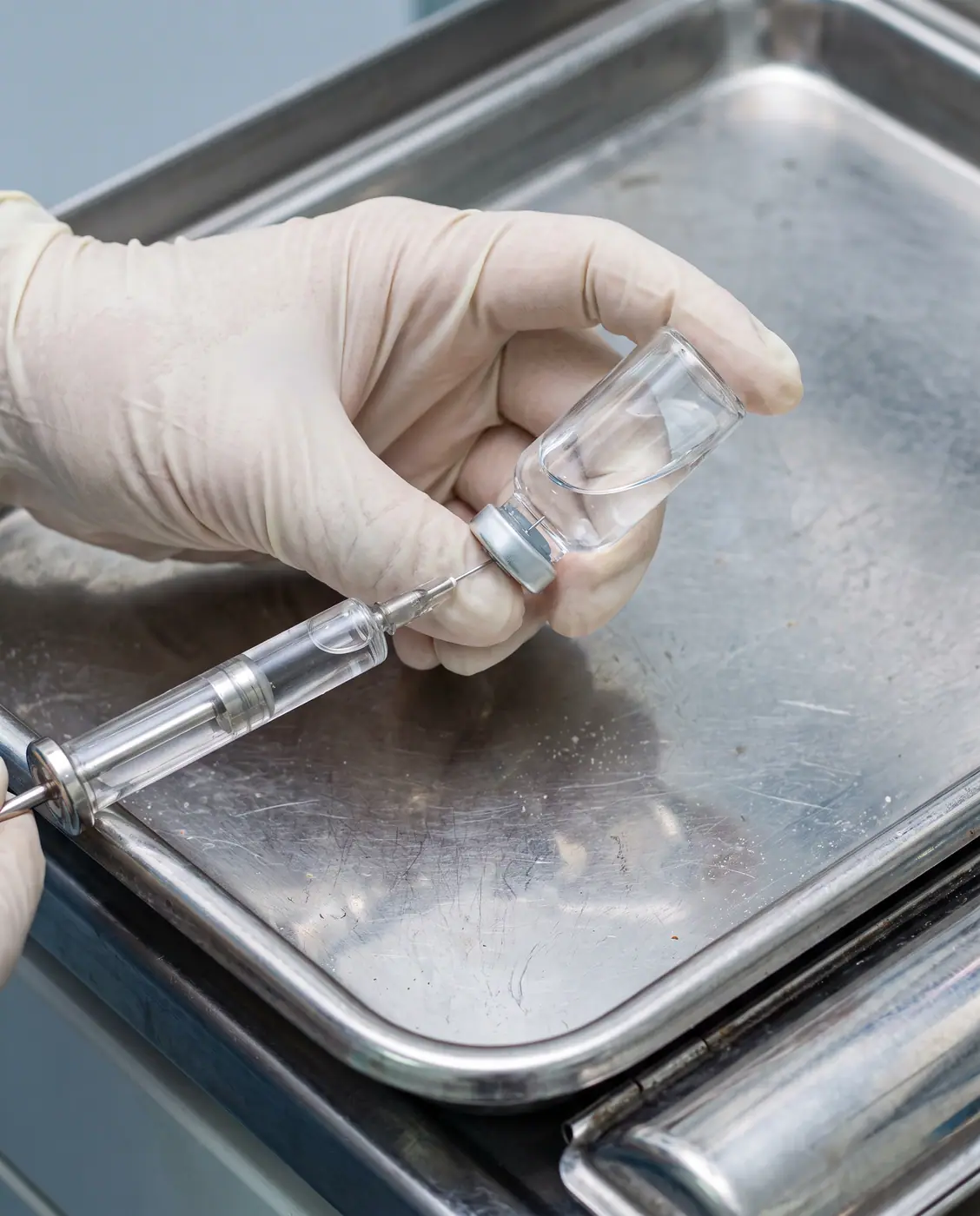 Close-up of a gloved hand preparing a syringe with clear liquid from a glass vial in a sterile