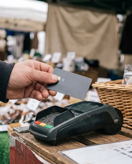 Hand using a contactless credit card on a payment terminal at a market stall, showing modern
