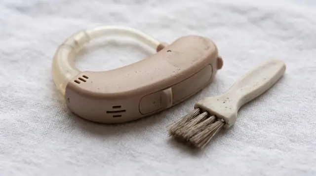 Extreme close-up of a behind-the-ear hearing aid and a small cleaning brush resting on a white
